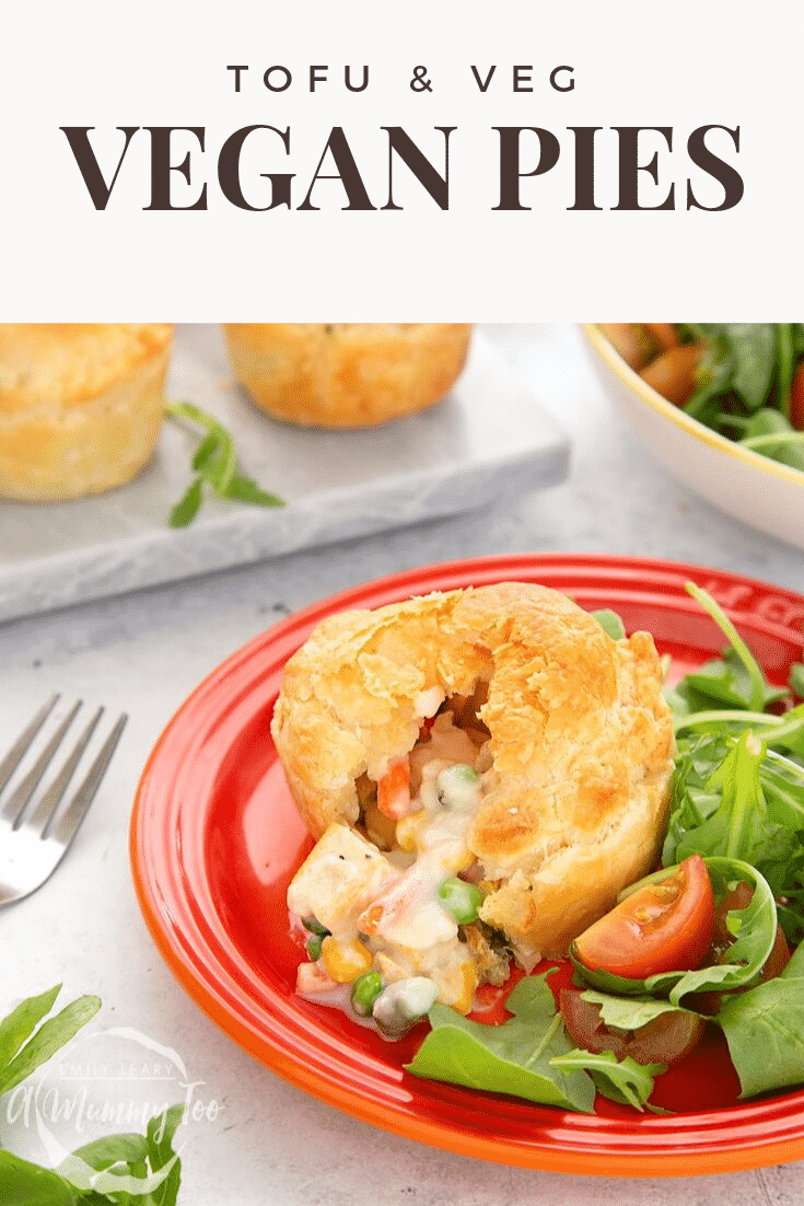 Side on view of a cut open vegan pie on a red plate with a salad on the side. In the background there's some additional pies on a marble chopping board. Meanwhile at the top of the image there's some brown text describing the image for Pinterest.
