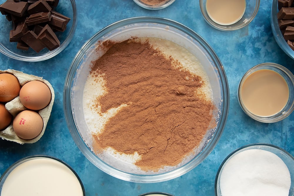 Drinking chocolate powder being added to the bowl of baileys cream topping ready for the baileys triple chocolate trifle