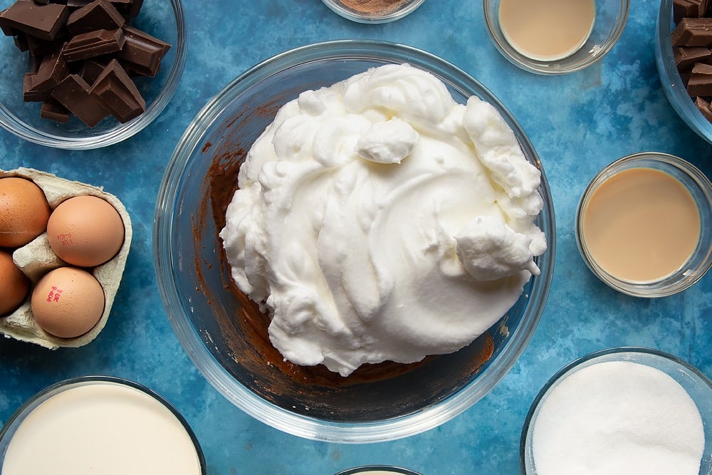 Egg whites being added to the baileys triple chocolate trifle ingredients in a bowl.