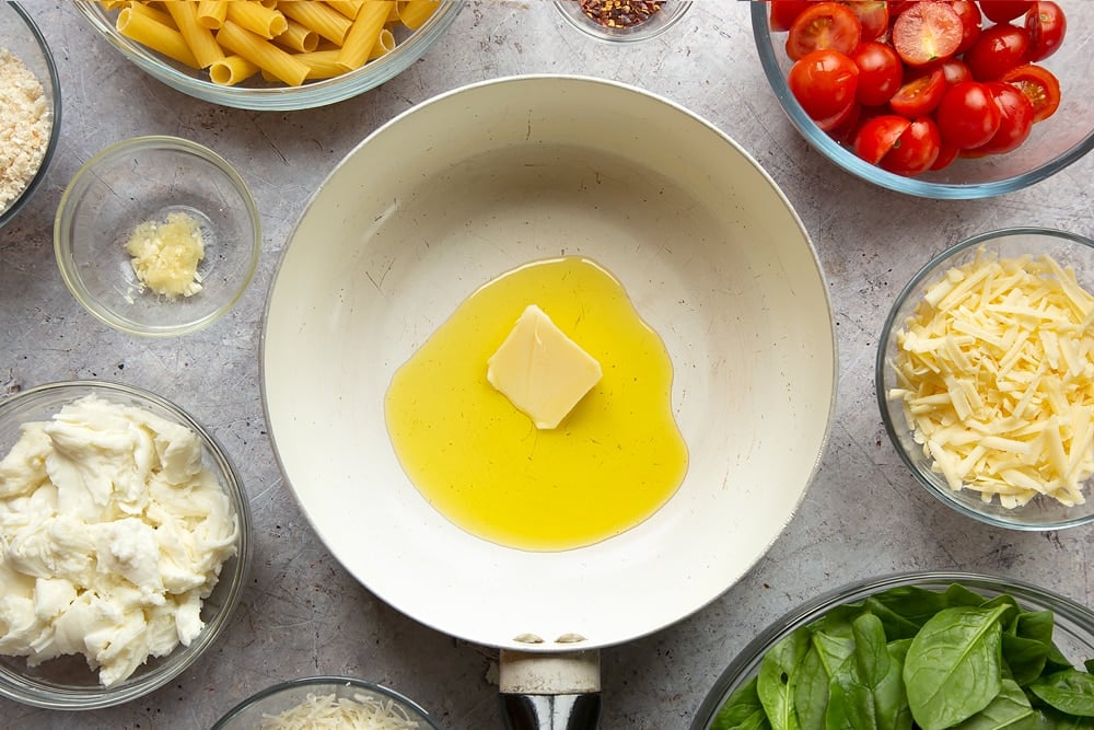 Butter melting in a pan surrounded by different ingredients required to make Cherry tomato, spinach and garlic mozzarella pasta bake. 