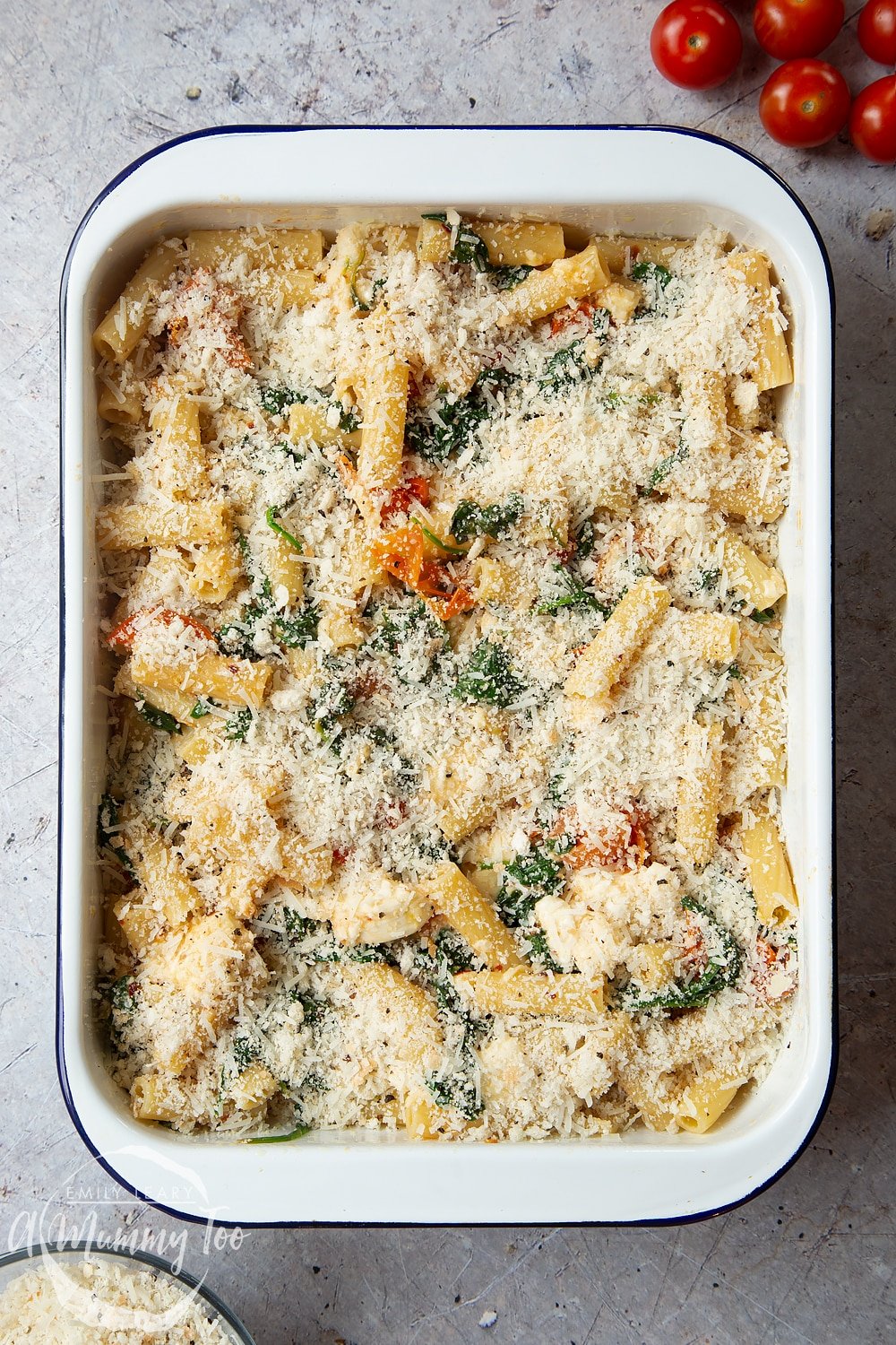Sprinkling the cheese over the Cherry tomato, spinach and garlic mozzarella pasta bake in a tray pan.
