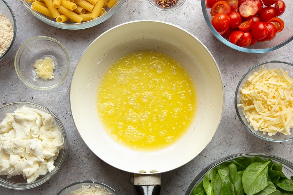 The butter having been melted in the pan. Surrounded by Cherry tomato, spinach and garlic mozzarella pasta bake ingredients. 