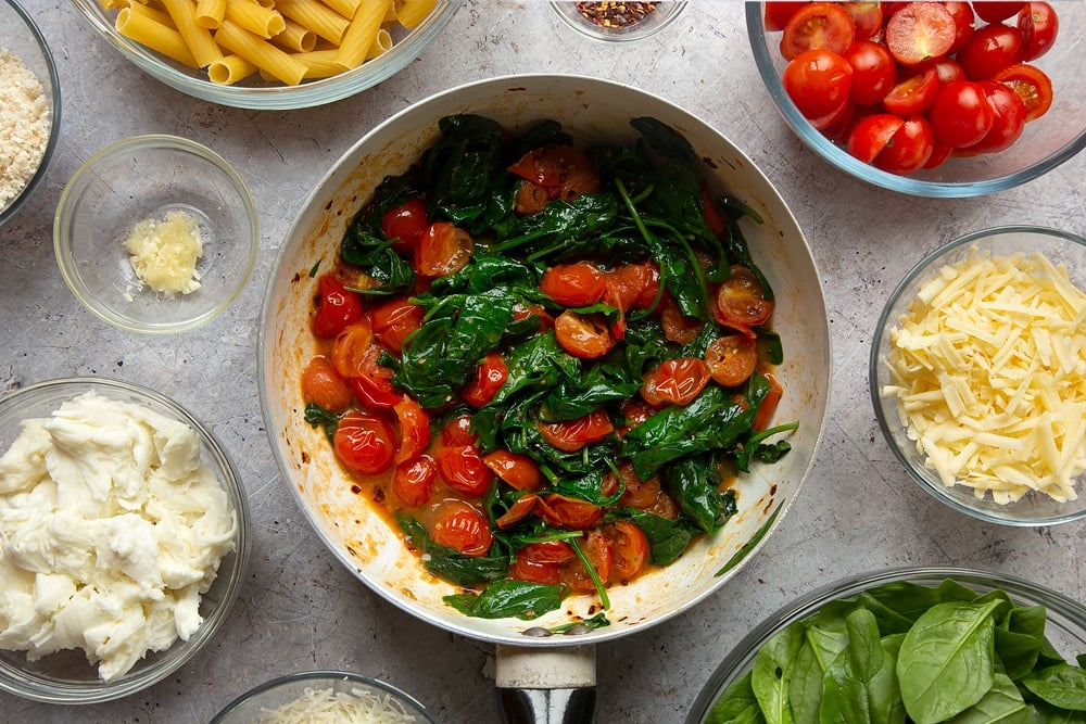 Spinach and tomatoes having been cooked in a pan. These are two of the ingredients required to make the Butter melting in a pan surrounded by different ingredients required to make Cherry tomato, spinach and garlic mozzarella pasta bake. 