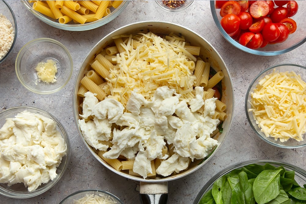 Cheeses being added to the pan of semi cooked pasta. Surrounded by additional ingredients required to make the Butter melting in a pan surrounded by different ingredients required to make Cherry tomato, spinach and garlic mozzarella pasta bake. 