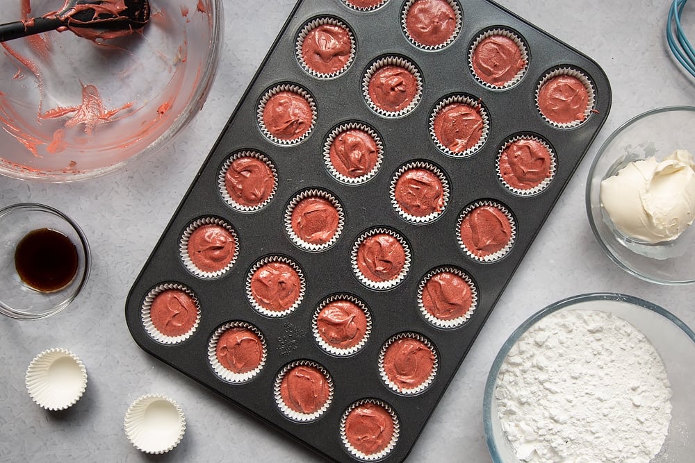 Overhead shot of lining a cupcake tray with cupcake liners and filling it with the cake mixture to make the mini red velvet cupcakes with cream cheese frosting. 