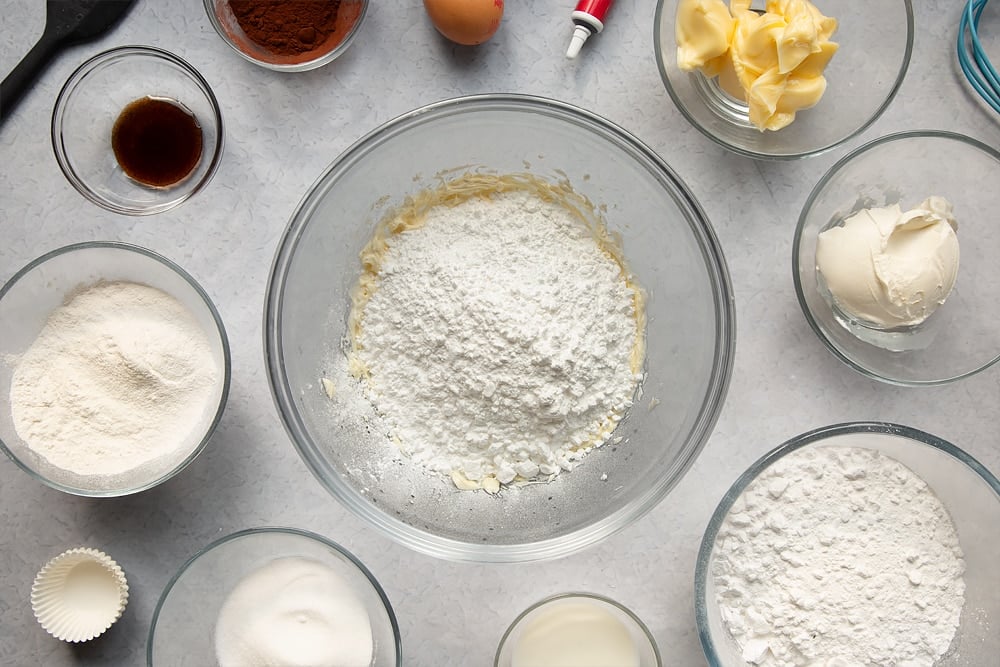 Adding icing sugar to the bowl of ingredients to make the cream cheese frosting. 