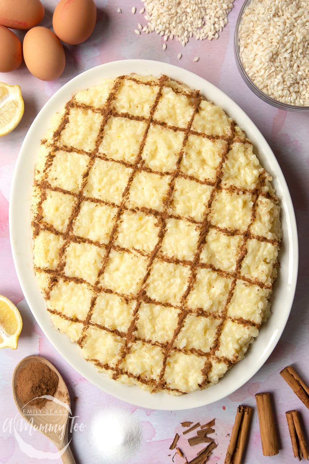 Arroz Doce (Portuguese rice pudding) on a large, white, oval-shaped plate. The rice pudding is decorated with ground cinnamon in a crosshatch pattern. 