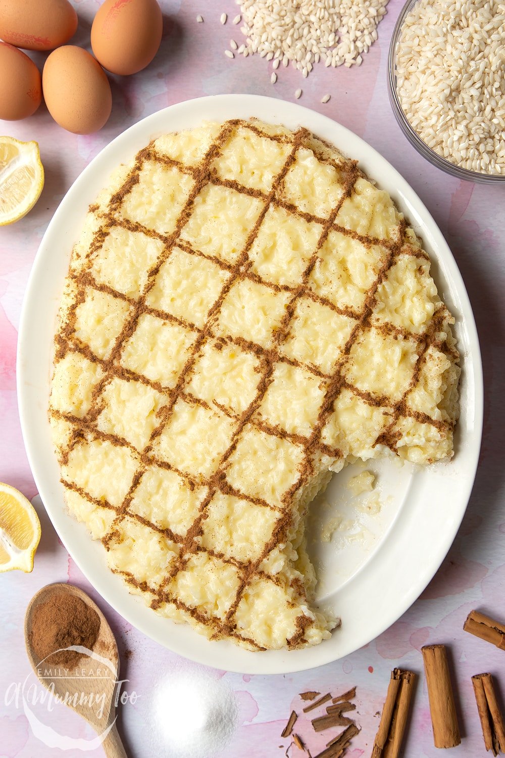 Arroz Doce (Portuguese rice pudding) on a large, white, oval-shaped plate. The rice pudding is decorated with ground cinnamon in a crosshatch pattern. Some of the pudding has been taken away.