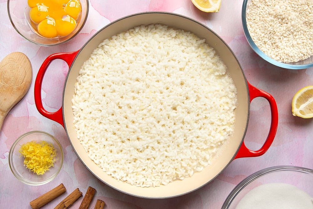 A pan filled with cooked arborio rice. Around the pan is the ingredients to make Arroz Doce.