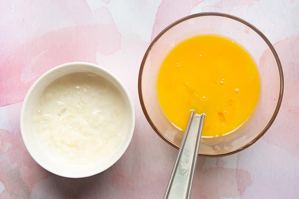 A small bowl containing a small amount of Arroz Doce, and a smaller bowl containing beaten egg yolks.