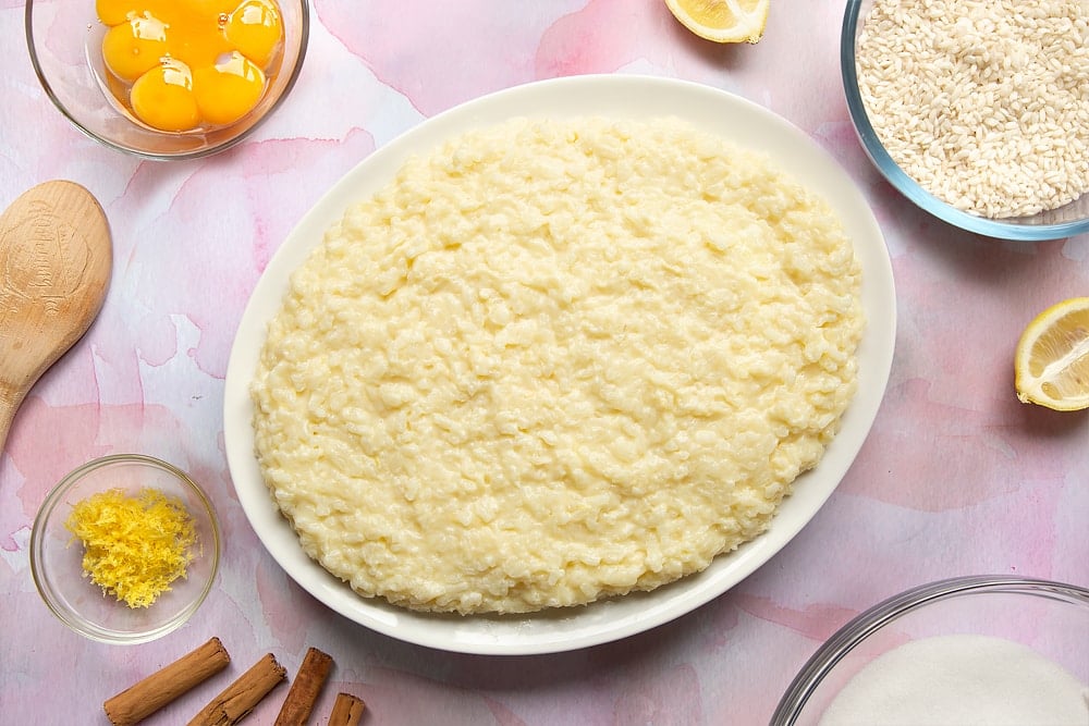 Arroz Doce served onto a white oval plate. Ingredients to make the rice pudding surround the plate.