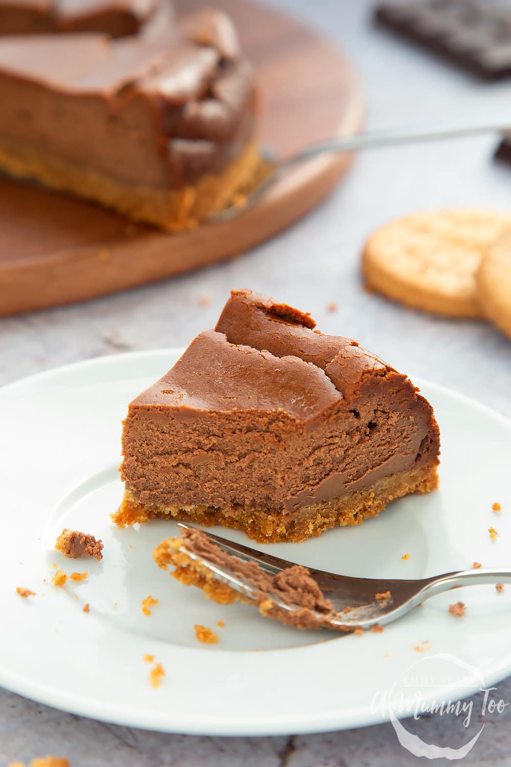 A white plate with a slice of baked chocolatew cheesecake. In the background there's some additional baked chocolate cheesecake slices.