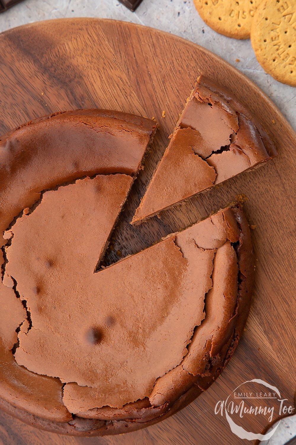 Overhead shot of the baked chocolate cheesecake on a wooden board. One slice of the cheesecake has been cut out.