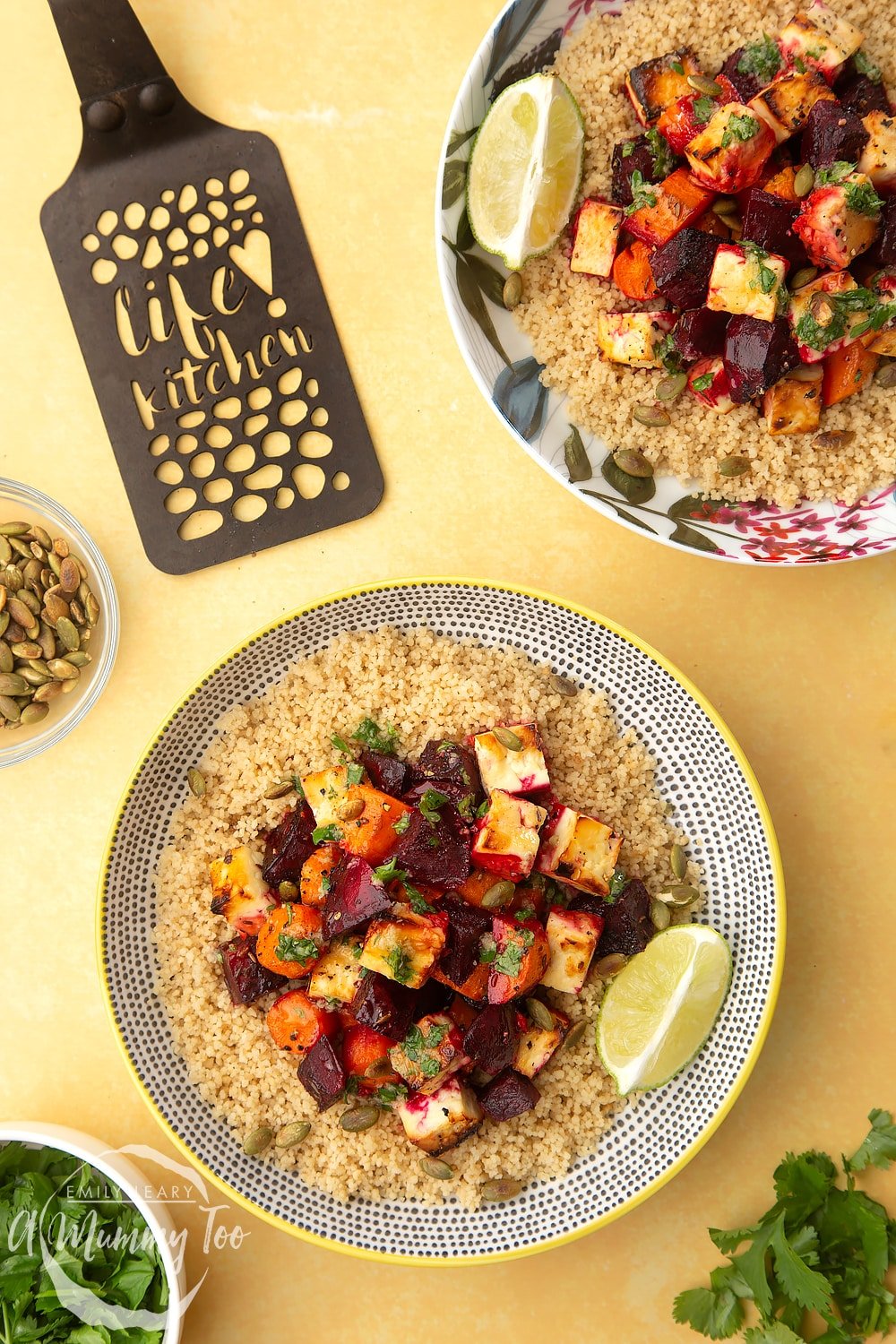 Overhead shot of two bowls with Beetroot and feta salad with couscous next to a decoative spaticular on top of a yellow table. 