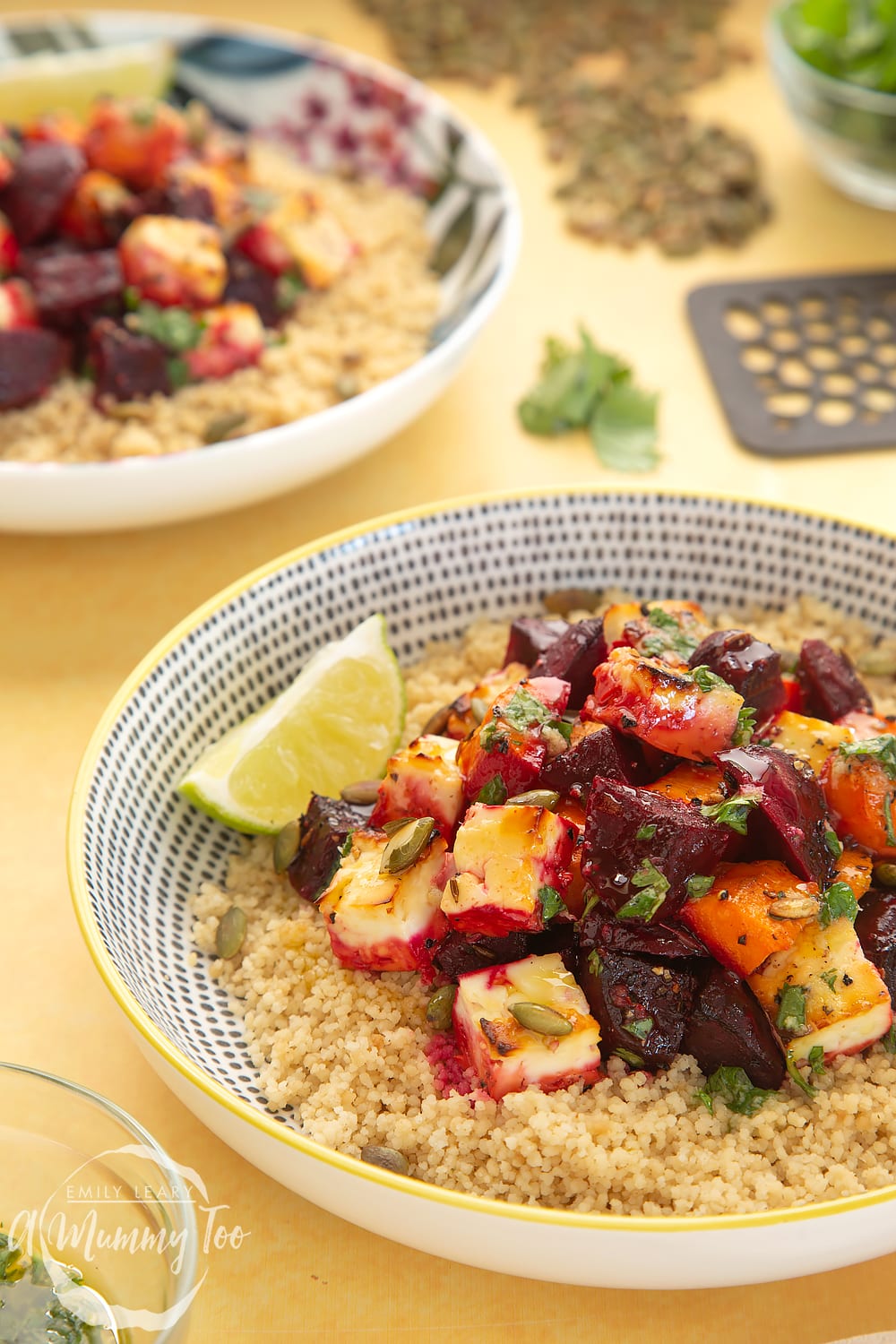 Ontop of a yellow table sits a decorative bowl filled with Beetroot and feta salad with couscous. 