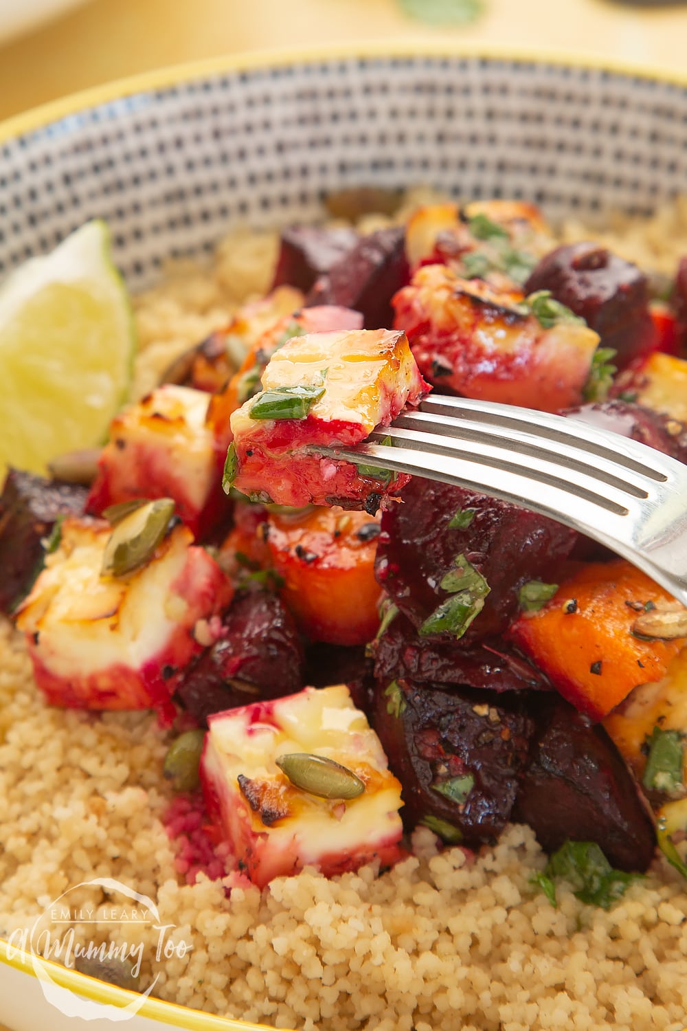 Close up of the beatroot on a fork coming out of a decorative yellow, black and white bowl filled with Beetroot and feta salad with couscous. 