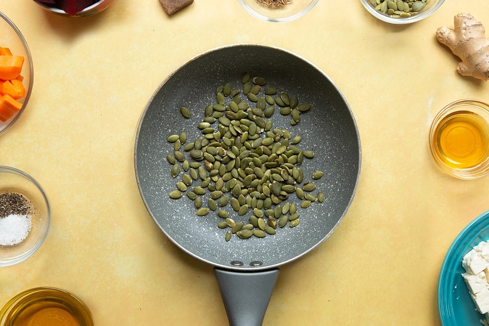 Overhead shot of a pan with pumpkin seeds sat on a yellow table.