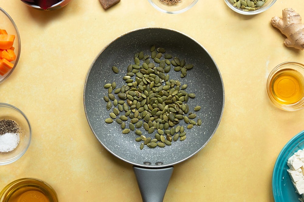 Overhead shot of a pan with pumpkin seeds sat on a yellow table. 