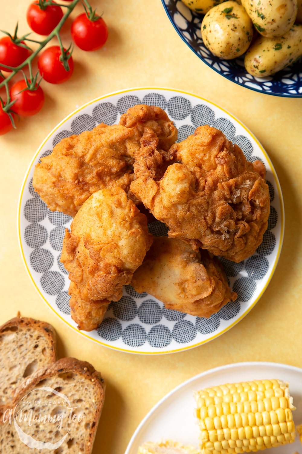 Gordon Ramsay’s buttermilk fried chicken arranged on a plate, surrounded by tomatoes, potatoes, bread and corn on the cob.