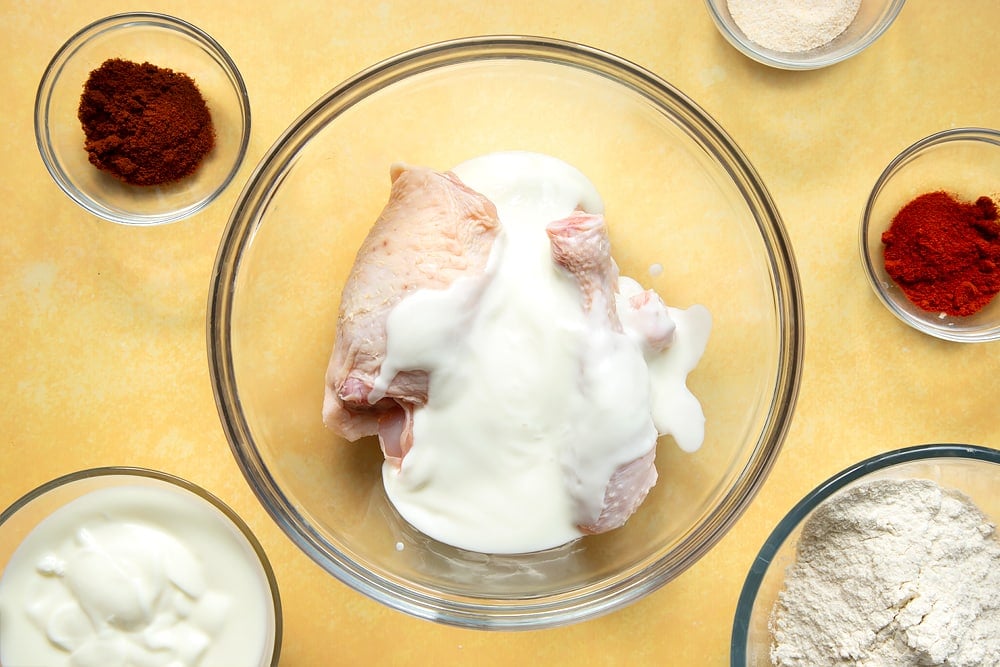 Chicken thighs and drumsticks in a large bowl, covered with buttermilk.