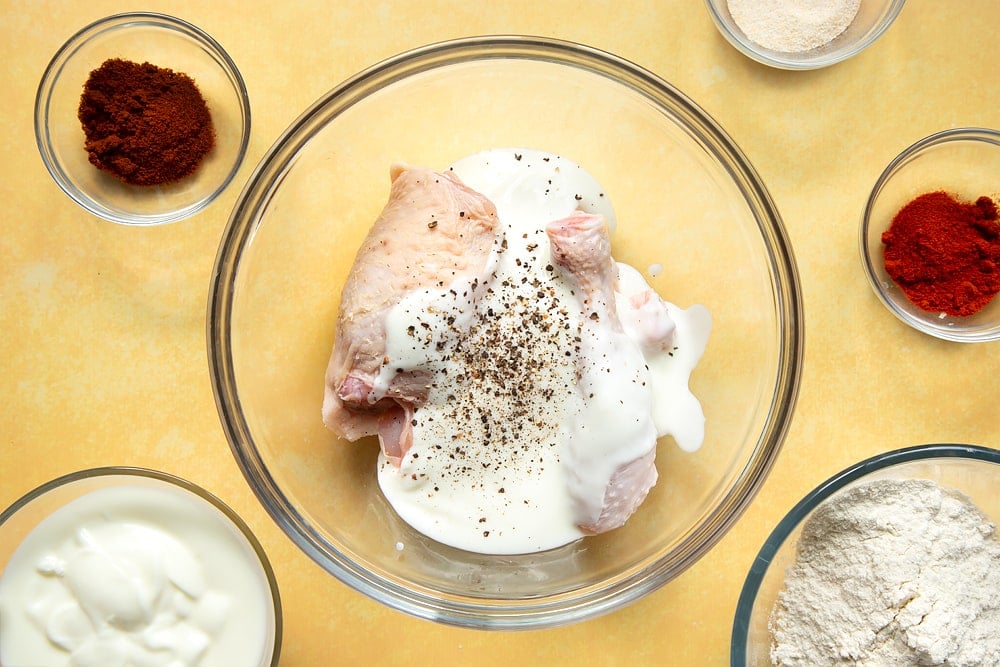 Chicken thighs and drumsticks in a large bowl, covered with buttermilk plus salt and pepper.