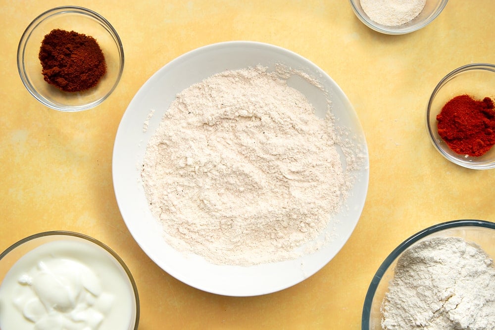 Flour mixed with paprika, garlic powder, cayenne pepper, salt and pepper on a plate.