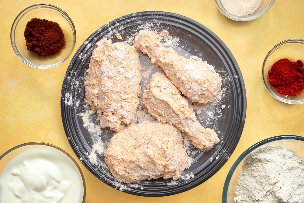 Chicken thighs and drumsticks on a plate, coated in buttermilk and then dipped in a flour mix containing with paprika, garlic powder, cayenne pepper, salt and pepper.