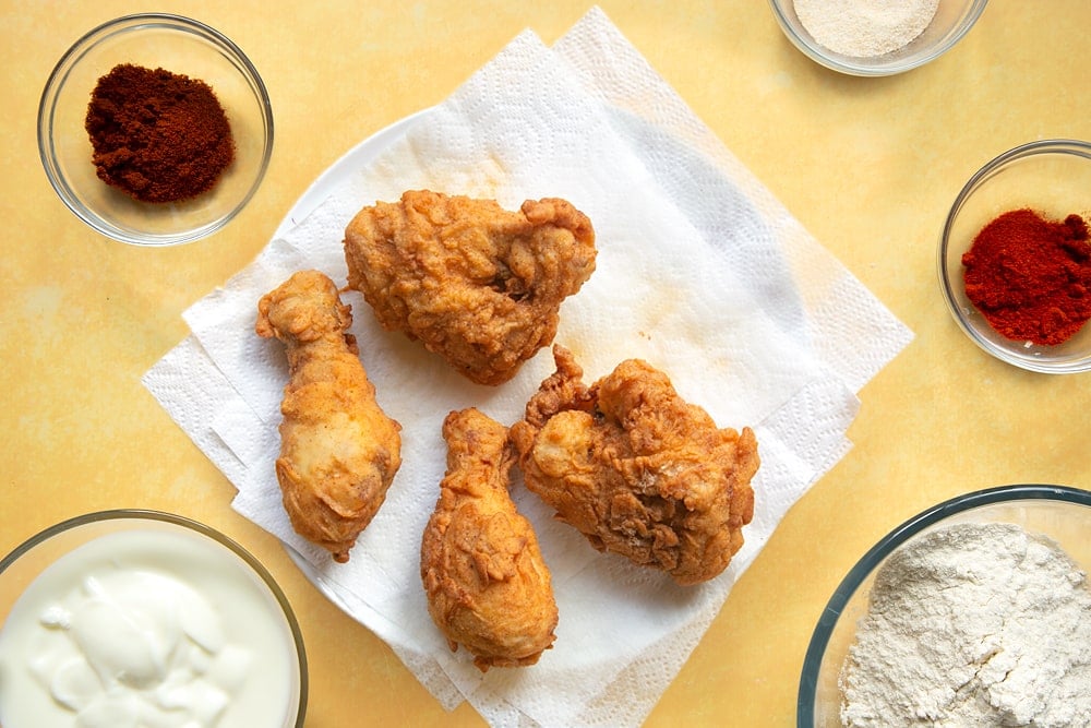 Buttermilk, flour and spice coated chicken thighs and drumsticks, fried and placed on a plate lined with kitchen roll to drain.