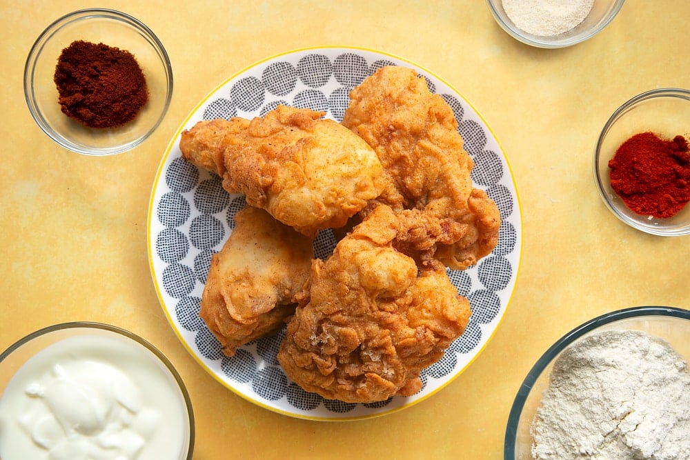 Freshly cooked buttermilk fried chicken on a patterned plate, surrounded by ingredients.