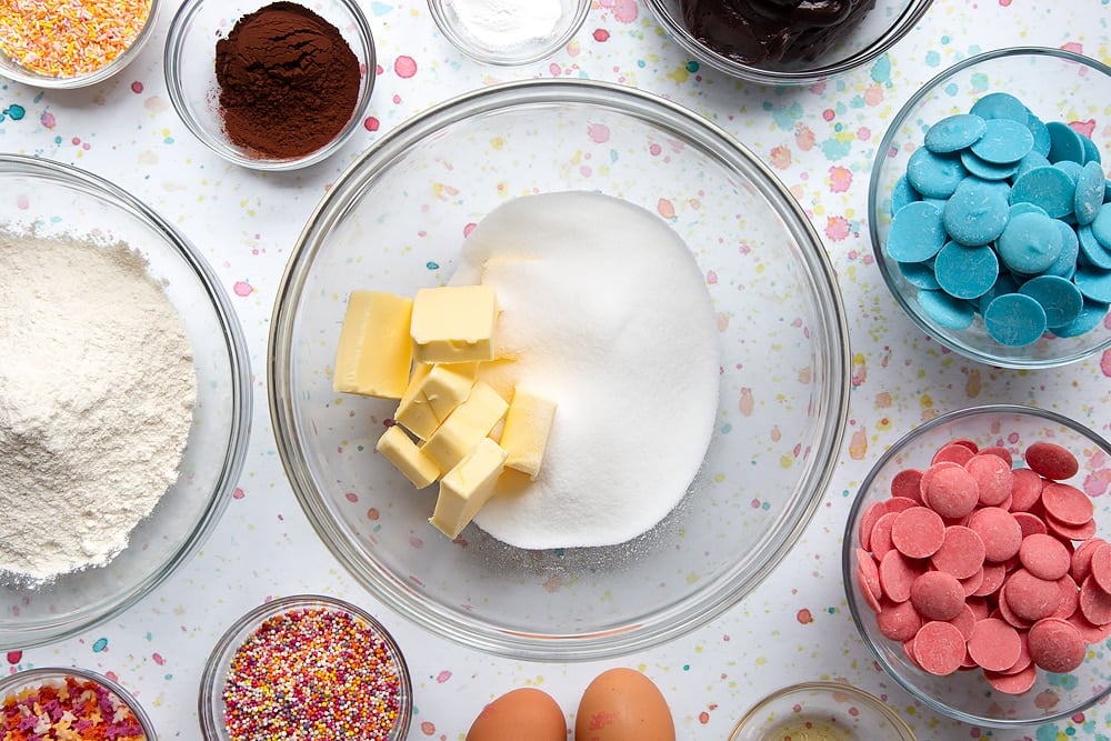  Sucre et beurre en cubes dans un bol. Les ingrédients pour faire un bouquet de cake pop entourent le bol.