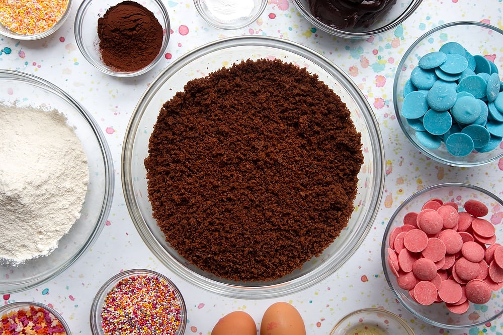 Chocolate cake crumbled in a bowl. Ingredients to make a cake pop bouquet surround the bowl.