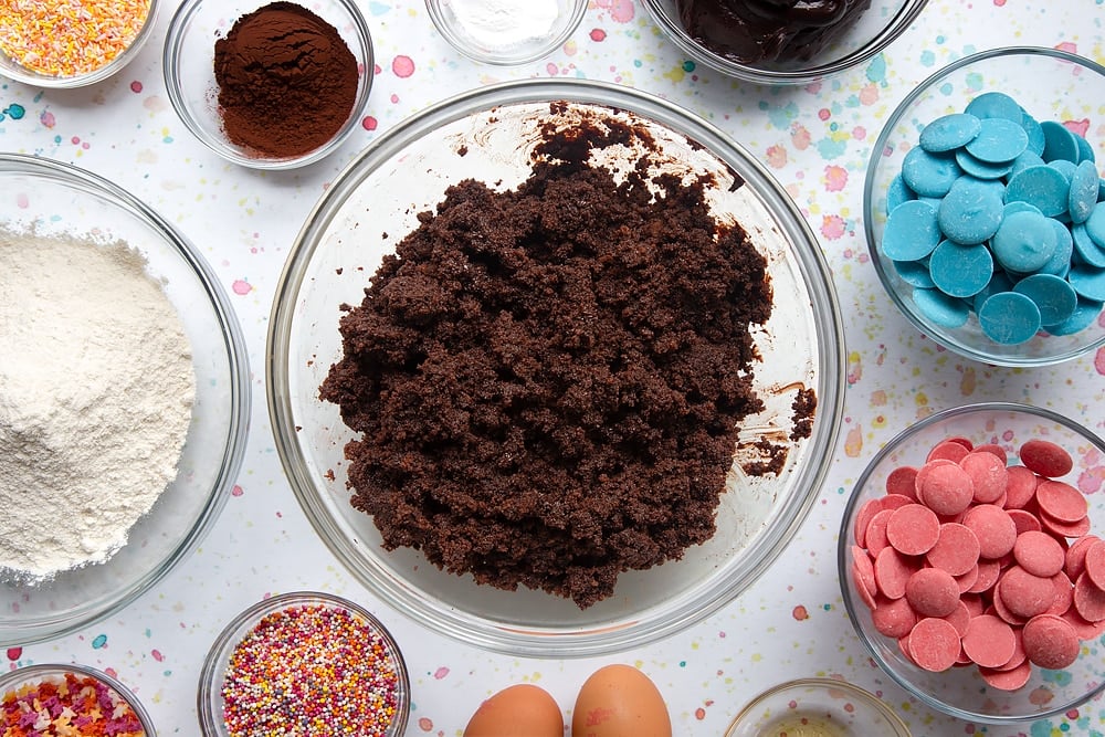 Schokoladenkuchen in einer Schüssel zerbröckelt und mit Schokoladenglasur vermischt. Zutaten für einen Cake Pop Bouquet umgeben die Schüssel.