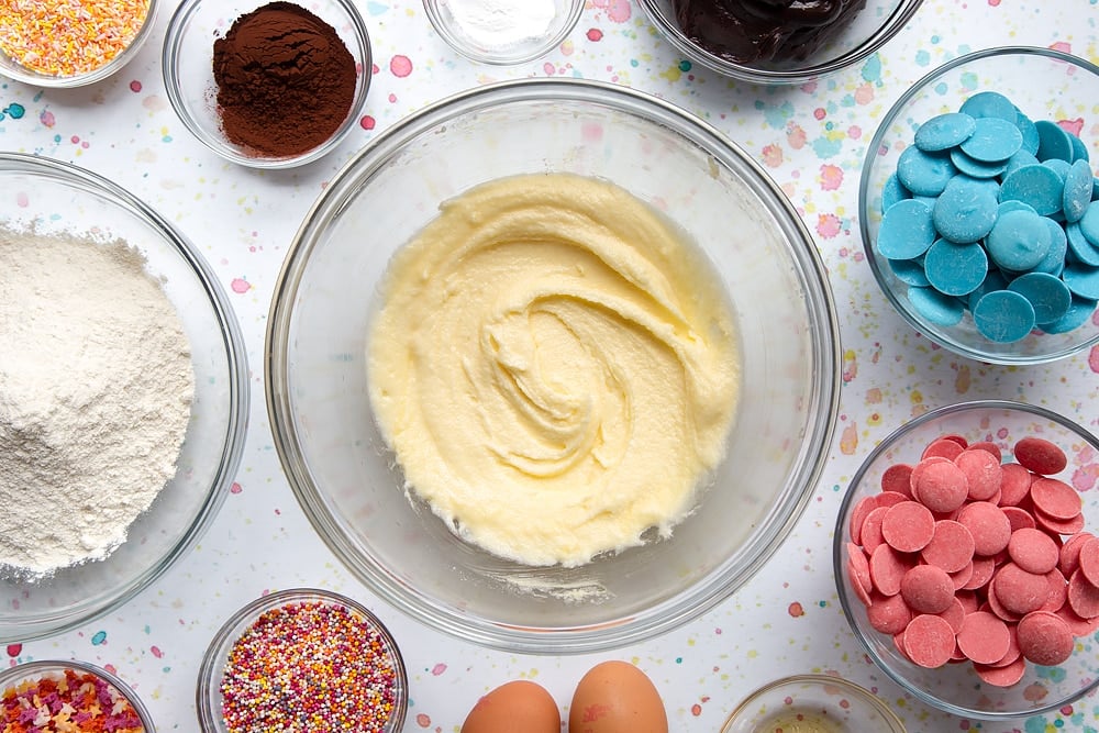 El azúcar y la mantequilla se mezclan en un bol. Los ingredientes para hacer un ramo de pastel rodean el tazón.