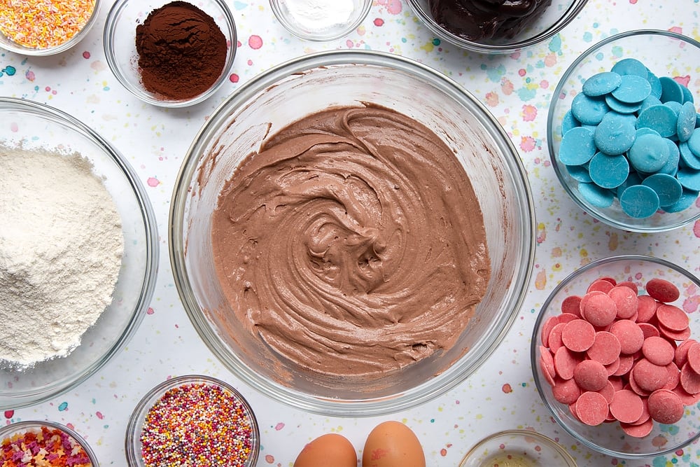 Chocolate cake batter in a bowl. Ingredients to make a cake pop bouquet surround the bowl.