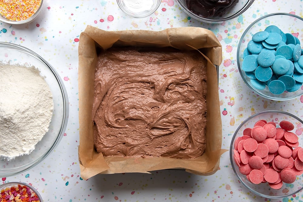 Chocolate cake batter in a baking tin lined with baking powder. Ingredients to make a cake pop bouquet surround the tin.