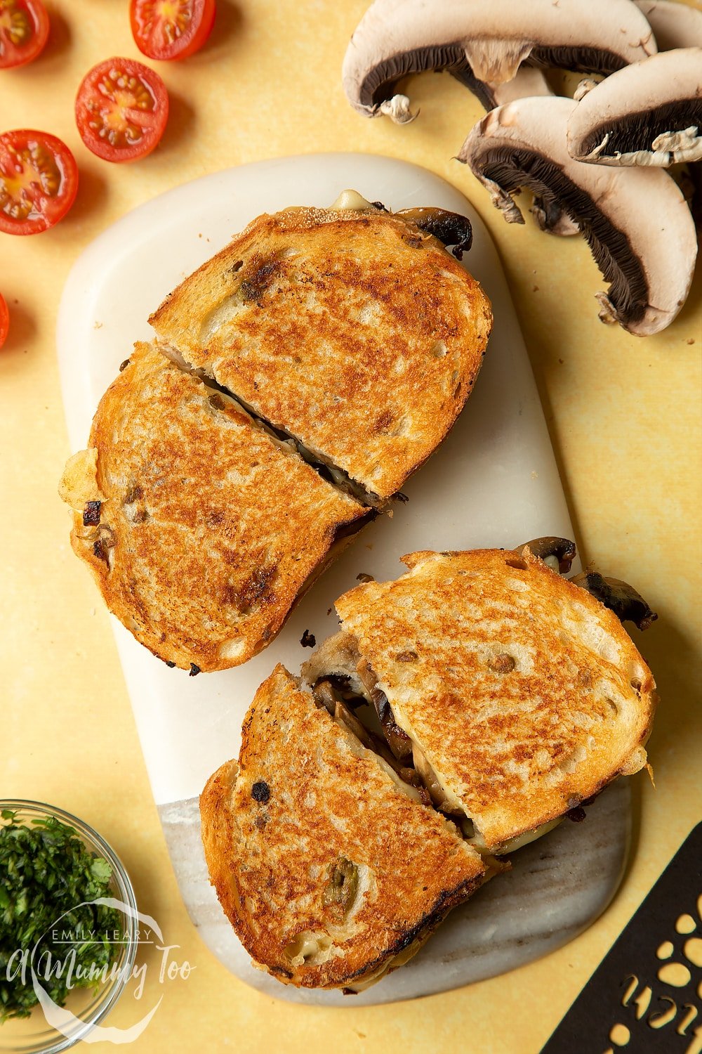 Two Jarlsberg cheese and mushroom toasties are on a serving board, both cut in half.