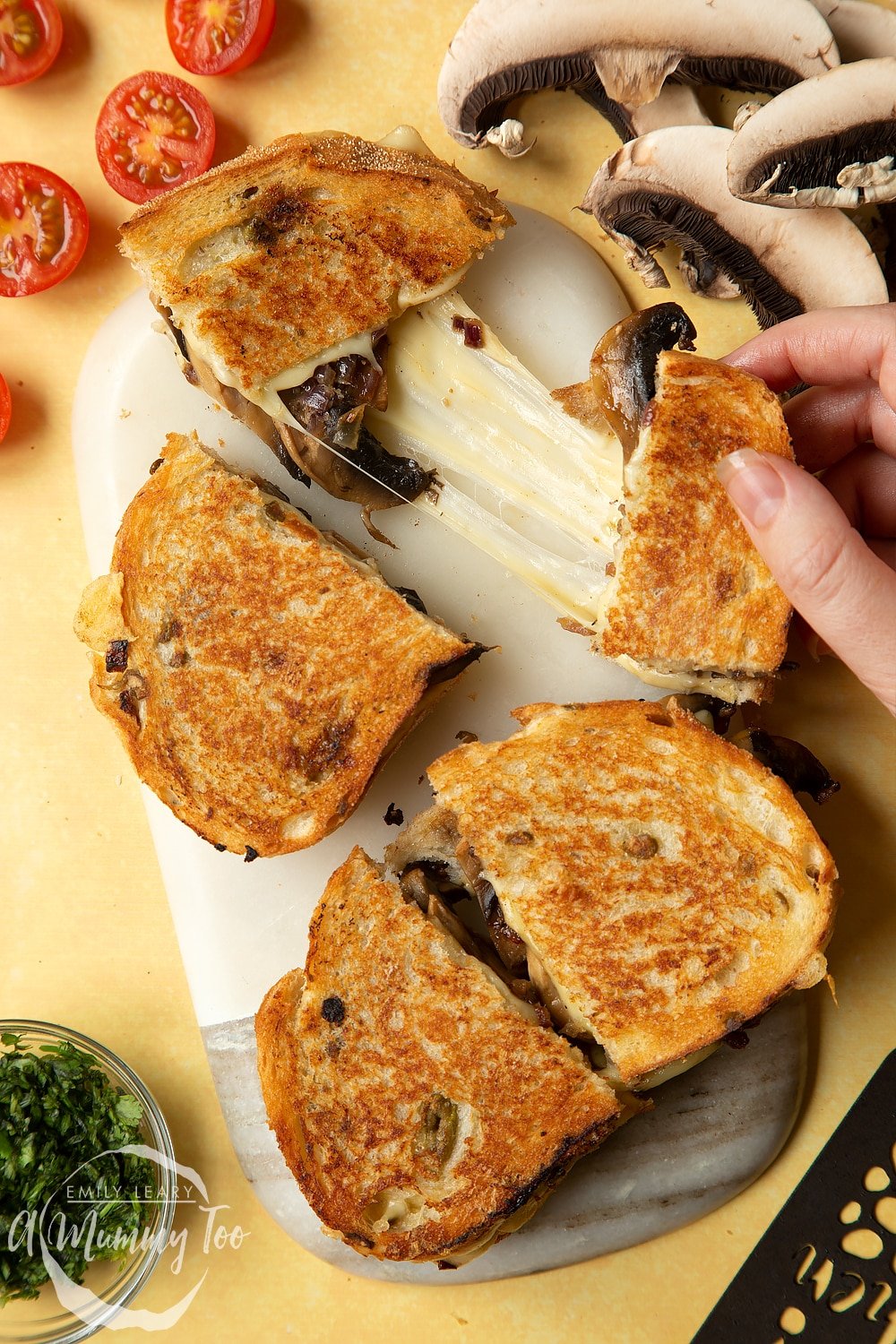 Two Jarlsberg cheese and mushroom toasties are on a serving board, one is being pulled apart very wide, the cheese is stretching between them almost to the point of breaking.