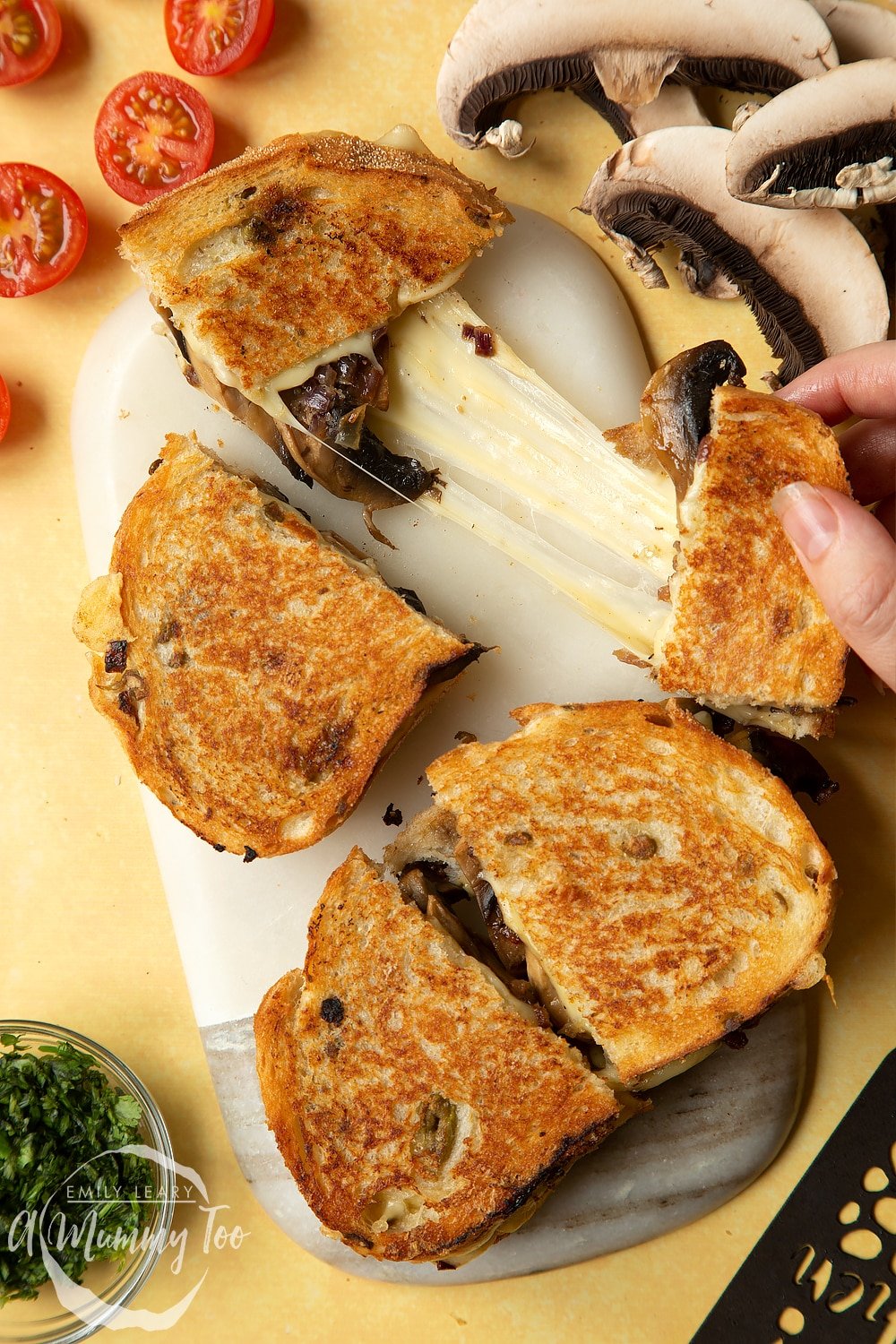 Two Jarlsberg cheese and mushroom toasties are on a serving board, one is being pulled apart so the cheese stretches out between them.