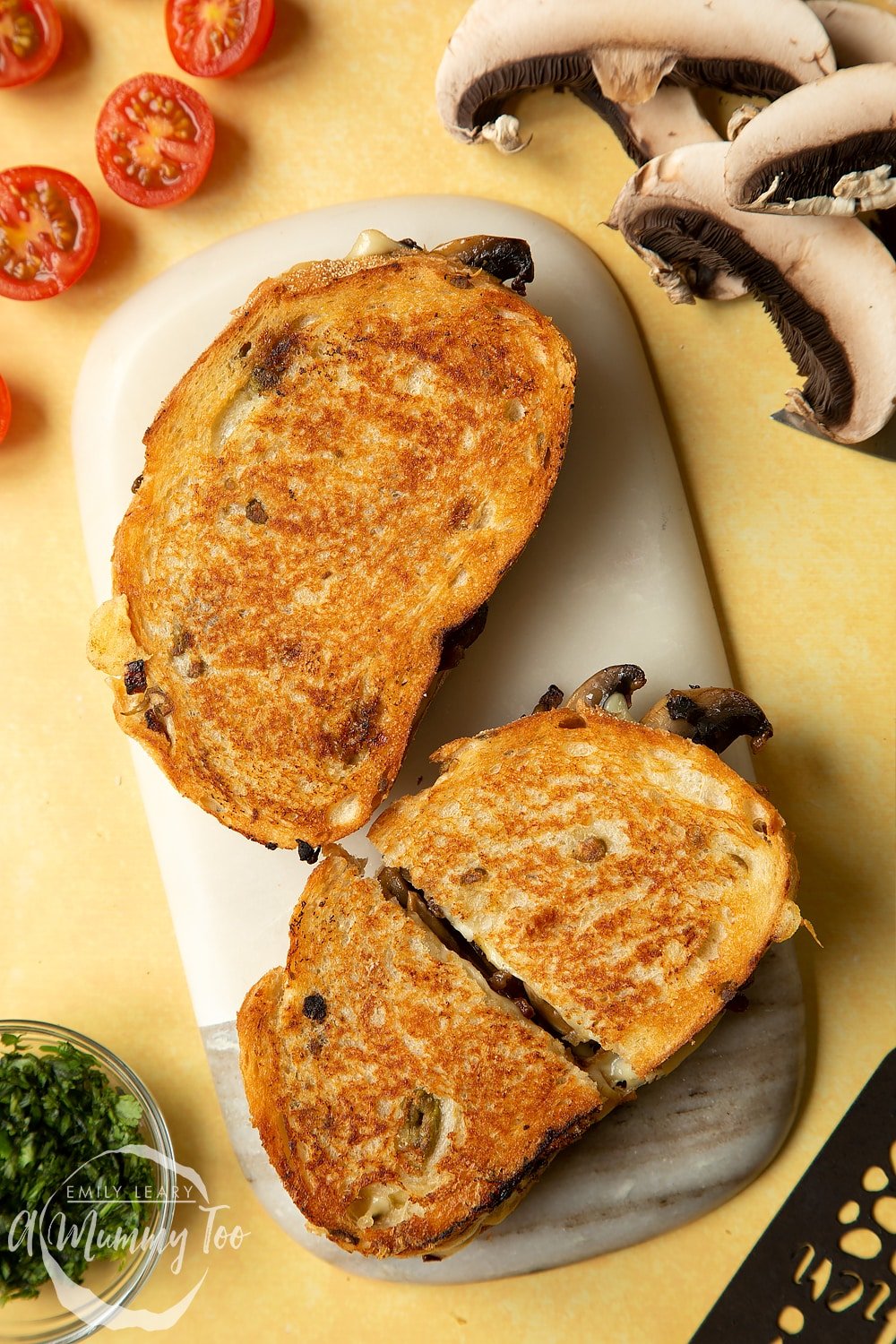 Two Jarlsberg cheese and mushroom toasties are on a serving board, one is cut in half.