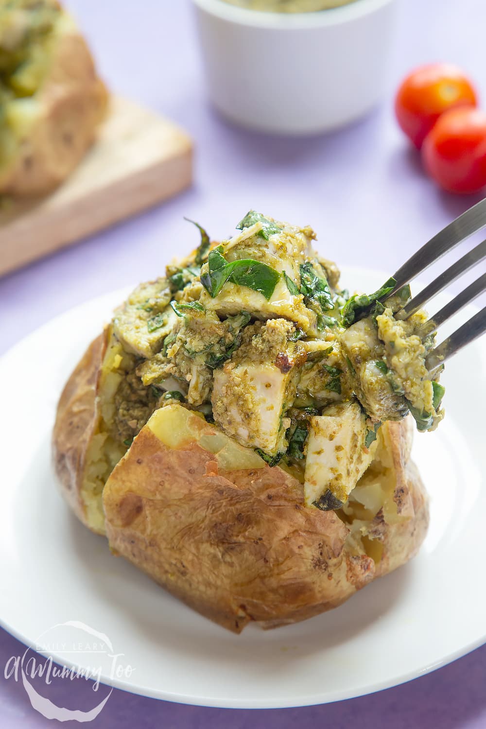 Jacket potato with cheesy pesto chicken on a white plate. The potato is piled high with a pesto, spinach cheese and chicken mix. A fork delves in.