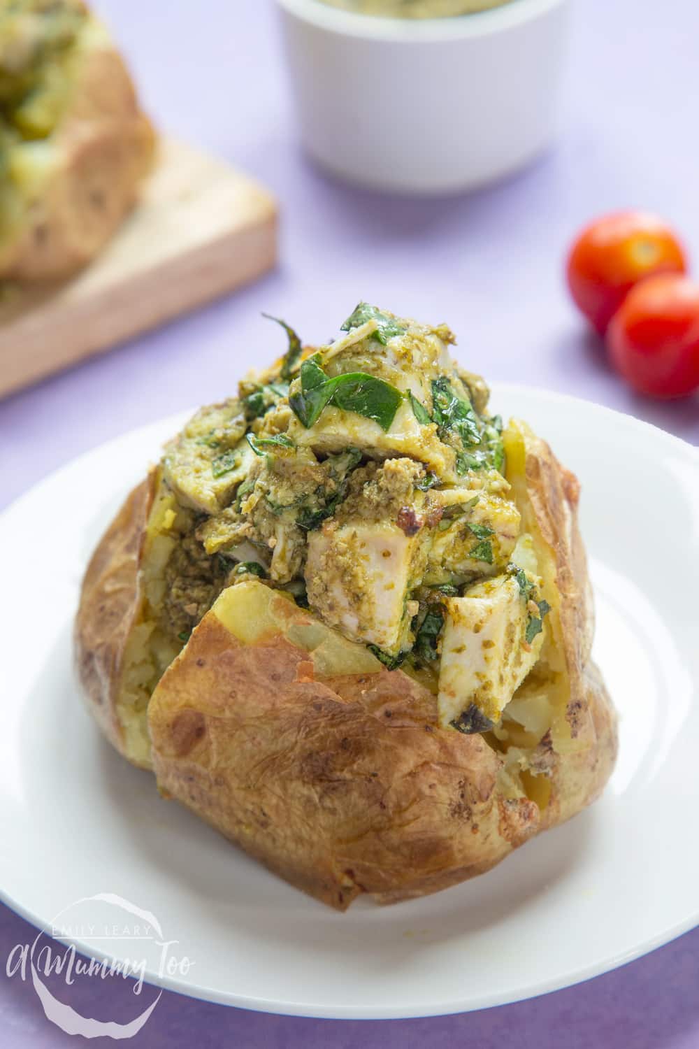 Jacket potato with cheesy pesto chicken on a white plate. The potato is piled high with a pesto, spinach cheese and chicken mix.