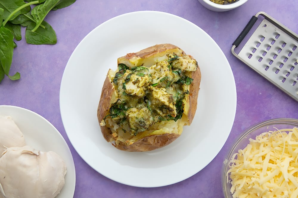 A jacket potato with cheesy pesto chicken served onto a white plate.