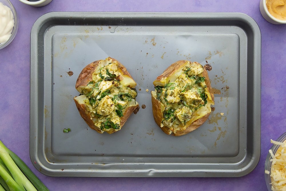 Freshly baked jacket potatoes with cheesy pesto chicken on a baking tray.