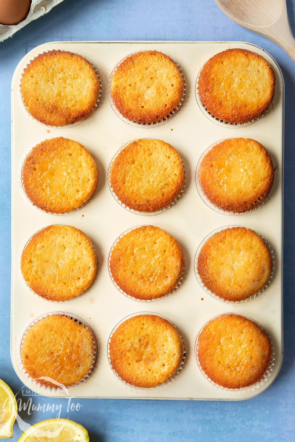 Lemon drizzle cupcakes in a cream-coloured muffin tray. 