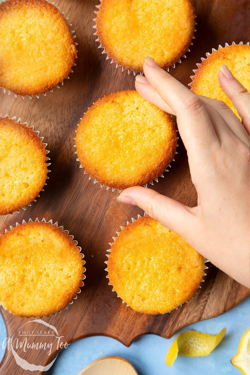 Lemon drizzle cupcakes on a wooden board. A hand reaches for one.