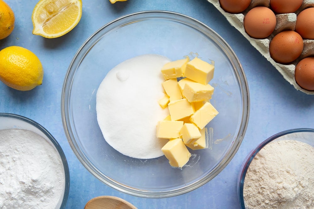 Butter and sugar in a glass mixing bowl, surrounded by ingredients to make lemon drizzle cupcakes.