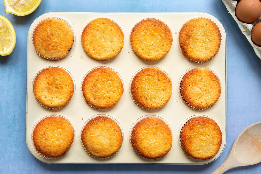 Lemon drizzle cupcakes in a cream-coloured muffin tray. 