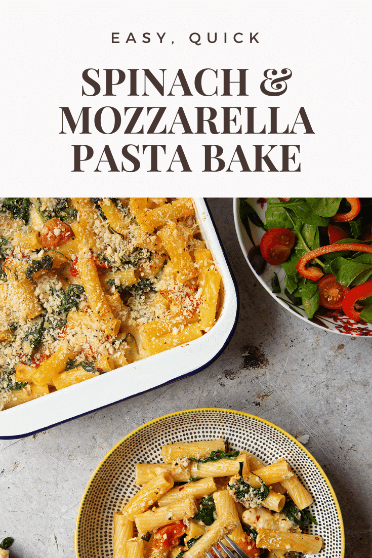 Overhead shot of a bowl of Cherry tomato, spinach and garlic mozzarella pasta bake alongside a side salad on a grey table. 