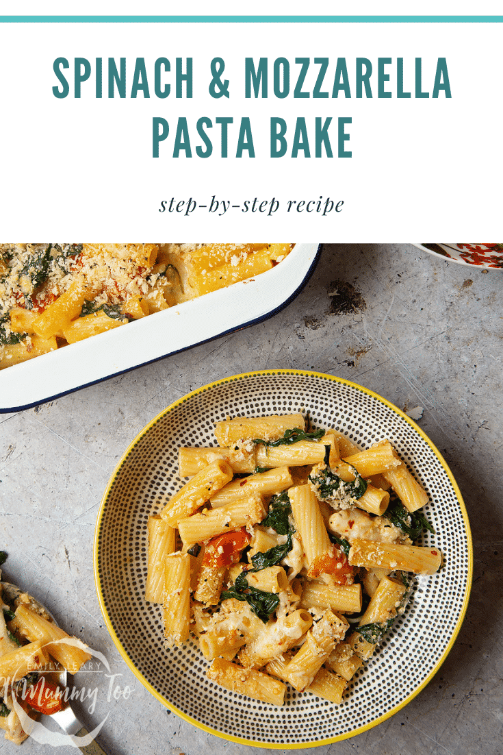 Overhead shot of a decorative bowl of Cherry tomato, spinach and garlic mozzarella pasta bake on a grey table. 