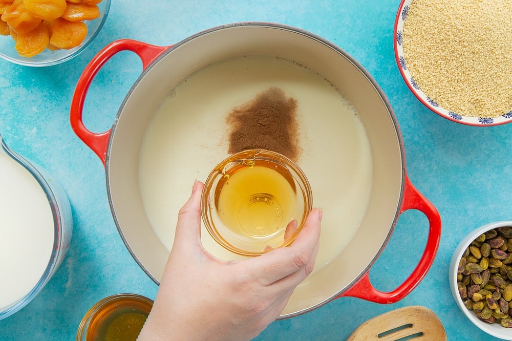 Overhead shot of the honey being added to the red pan of sweet breakfast couscous ingredients. 